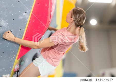 Woman doing difficult wall climb in climbing gym 131927917