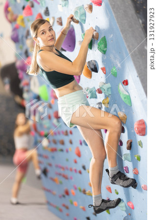 Woman climbs artificial wall bouldering, working out in gym 131927923