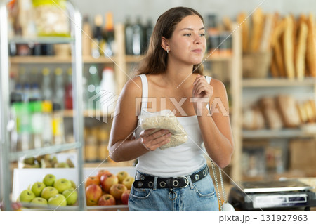 In grocery supermarket, female shopper chooses oat flakes for breakfast 131927963