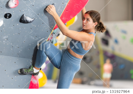 Girl climbs artificial wall bouldering, working out in gym Girl climbs artificial wall bouldering, working out in gym 131927964