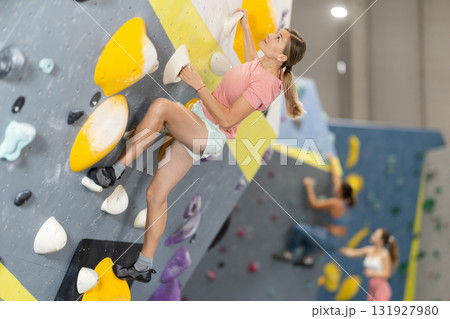 Woman climbs artificial wall bouldering, working out in gym 131927980