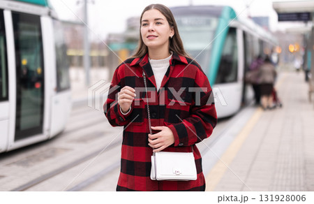 Girl is standing on street platform, waiting for tram to arrive Girl is standing on street platform, waiting for tram to arrive 131928006