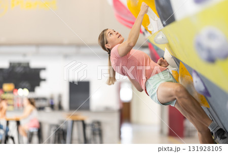Woman climbs artificial wall bouldering, working out in gym 131928105