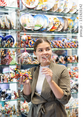 Satisfied young woman chooses traditional Spanish souvenirs - miniature mosaic figurine of bull Satisfied young woman chooses traditional Spanish souvenirs - miniature mosaic figurine of bull 131928142