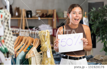 Girl with poster in hands announces mega discounts in womens clothing store. Girl with poster in hands announces mega discounts in womens clothing store. 131928178