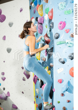 Girl climbs artificial wall bouldering, working out in gym Girl climbs artificial wall bouldering, working out in gym 131928179