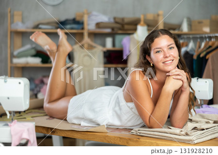 Young fashion designer lying on worktable barefoot in studio 131928210