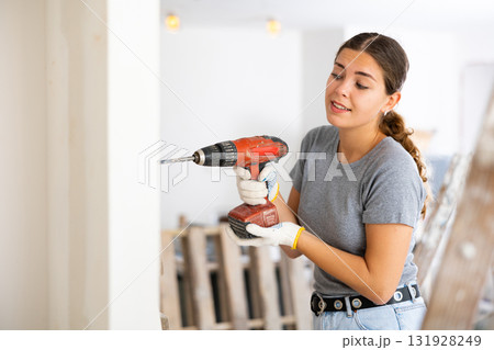 Woman drilling hole in wall with screwdriver in repairable room 131928249
