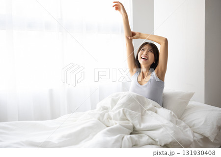 朝日を浴びながらベッドで伸びをする若い女性 朝日を浴びながらベッドで伸びをする若い女性 131930408