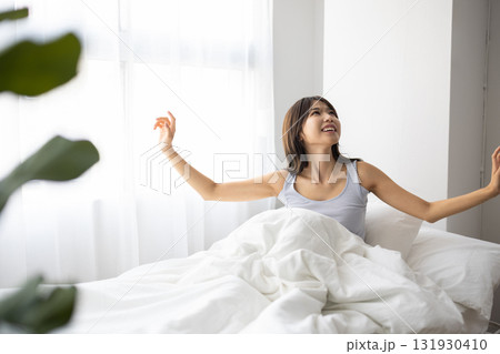 ベッドで起き上がり微笑む若い女性 ベッドで起き上がり微笑む若い女性 131930410