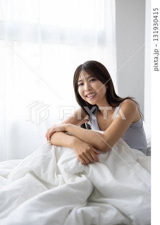 ベッドで起き上がり微笑む若い女性 ベッドで起き上がり微笑む若い女性 131930415