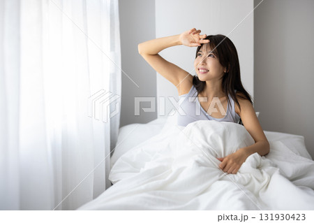 ベッドで起き上がり微笑む若い女性 ベッドで起き上がり微笑む若い女性 131930423