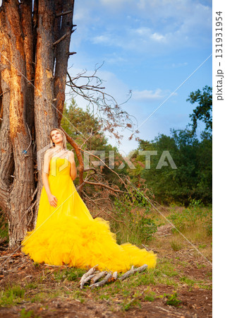 An Elegant Woman Dressed in a Beautiful Yellow Dress is Standing Gracefully by a Tree 131931954