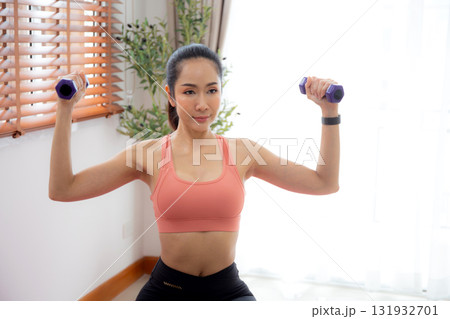 Young asian woman in sportswear workout with dumbbells for strength in living room. 131932701