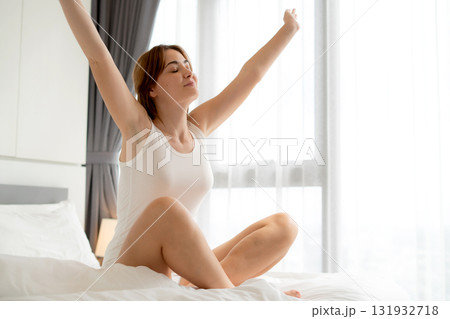 Happy young caucasian woman stretching hand on bed in morning, wellness lifestyle routine. 131932718