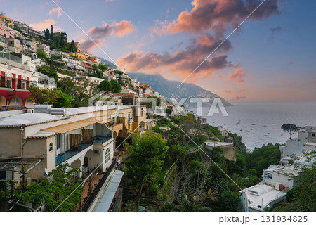 The town of Positano, Italy, features colorful terraced buildings on a hillside, with sunset skies, the Tyrrhenian Sea, boats, and lush greenery. The town of Positano, Italy, features colorful terraced buildings on a hillside, with sunset skies, the Tyrrhenian Sea, boats, and lush greenery. 131934825