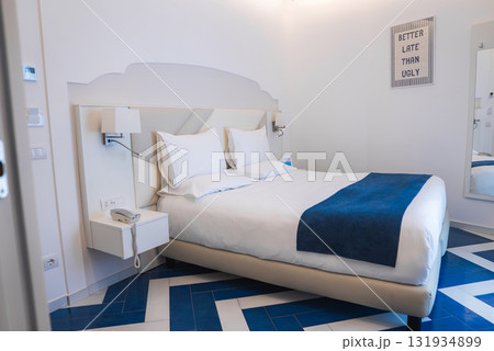 Stylish hotel room in Amalfi, Italy, featuring a minimalist design, blue chevron patterned tiles, white linens, and a wall mounted nightstand. 131934899