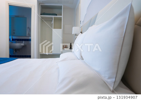A minimalistic hotel room featuring a neatly made bed, open wardrobe with shelves, and a bathroom with blue and white tiled walls in Amalfi, Italy. 131934907