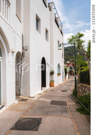A picturesque street on Capri, Italy, lined with whitewashed buildings, arched doorways, potted plants, and a lamppost, with hills in the background. A picturesque street on Capri, Italy, lined with whitewashed buildings, arched doorways, potted plants, and a lamppost, with hills in the background. 131935008