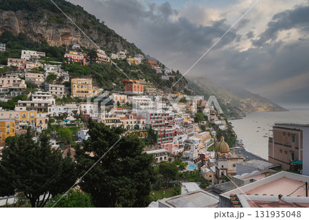 Positano on the Amalfi Coast features stacked buildings, a church dome, lush greenery, cliffs, and the Mediterranean Sea under a cloudy sky. Positano on the Amalfi Coast features stacked buildings, a church dome, lush greenery, cliffs, and the Mediterranean Sea under a cloudy sky. 131935048