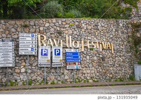 A stone wall in Ravello, Italy, displays the golden words 'Ravello Festival' above directional signs to Piazza Duomo, Scala, Amalfi, and parking areas. A stone wall in Ravello, Italy, displays the golden words 'Ravello Festival' above directional signs to Piazza Duomo, Scala, Amalfi, and parking areas. 131935049