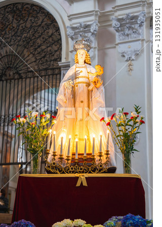 Statue of Virgin Mary with infant Jesus on a red velvet pedestal, surrounded by candles and flowers, set against a wrought iron gate in Ravello, Italy. 131935051