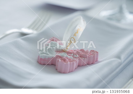 Decorative cross shaped ornament with floral details and angel motif on a folded napkin, with a fork and glass in a refined dining setting. 131935068