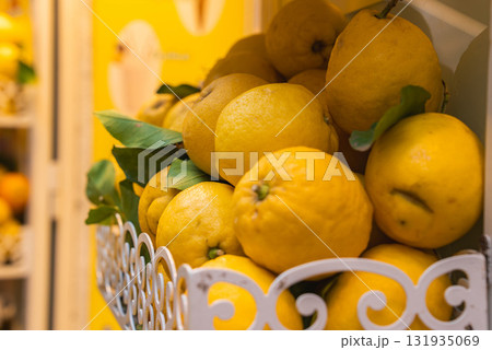Bright yellow lemons with green leaves sit in a decorative white metal basket. A yellow wall in the background complements the citrus display. Bright yellow lemons with green leaves sit in a decorative white metal basket. A yellow wall in the background complements the citrus display. 131935069