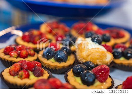 A close up view of fruit tarts with strawberries, blueberries, raspberries, and a cream filled pastry on a blue plate, showcasing Amalfi's culinary style. A close up view of fruit tarts with strawberries, blueberries, raspberries, and a cream filled pastry on a blue plate, showcasing Amalfi's culinary style. 131935133