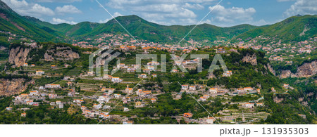 Aerial view of the Amalfi region in Italy, showcasing terraced hills, pastel colored buildings, rugged cliffs, and rolling green mountains under a cloudy sky. Aerial view of the Amalfi region in Italy, showcasing terraced hills, pastel colored buildings, rugged cliffs, and rolling green mountains under a cloudy sky. 131935303