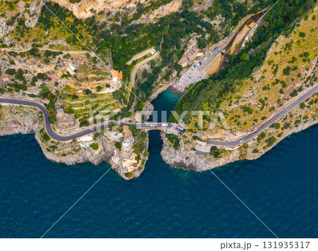 Aerial image of a narrow bridge over a small inlet on the Amalfi Coast, with cliffs, terraced greenery, buildings, and a secluded beach by the Tyrrhenian Sea. Aerial image of a narrow bridge over a small inlet on the Amalfi Coast, with cliffs, terraced greenery, buildings, and a secluded beach by the Tyrrhenian Sea. 131935317