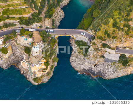 Aerial image of a bridge spanning a rocky gorge on the Amalfi Coast, Italy, with a luxury property, terraces, and pools overlooking the Tyrrhenian Sea. 131935320