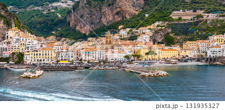 Aerial view of Amalfi, Italy, showing colorful hillside buildings, a domed church, dramatic cliffs, a pier, and the vibrant blue Tyrrhenian Sea. Aerial view of Amalfi, Italy, showing colorful hillside buildings, a domed church, dramatic cliffs, a pier, and the vibrant blue Tyrrhenian Sea. 131935327