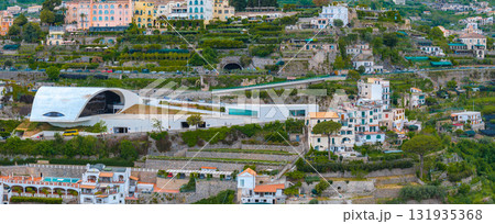 Aerial view of Ravello, Italy, featuring the curved white roof of the Auditorium Oscar Niemeyer, terraced hillsides, villas, and colorful buildings. Aerial view of Ravello, Italy, featuring the curved white roof of the Auditorium Oscar Niemeyer, terraced hillsides, villas, and colorful buildings. 131935368