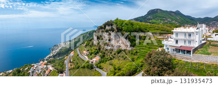 Aerial view of the Amalfi Coast in Italy, showing a white hotel on a terraced hillside, lush greenery, cliffs, winding roads, and the Tyrrhenian Sea. Aerial view of the Amalfi Coast in Italy, showing a white hotel on a terraced hillside, lush greenery, cliffs, winding roads, and the Tyrrhenian Sea. 131935473