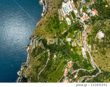 Aerial image of Amalfi town in Italy, featuring terraced hills, winding roads, a luxury hotel with a pool, and the blue Tyrrhenian Sea on the left. Aerial image of Amalfi town in Italy, featuring terraced hills, winding roads, a luxury hotel with a pool, and the blue Tyrrhenian Sea on the left. 131935555