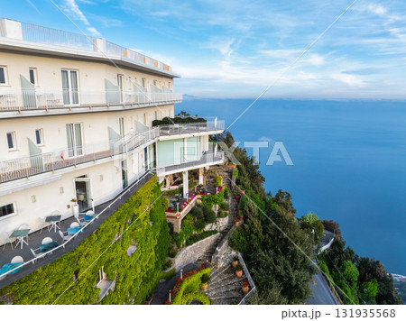 A cliffside hotel in Amalfi, Italy, with balconies, terraces, lush vegetation, a stone pathway, landscaped gardens, and views of the Tyrrhenian Sea. A cliffside hotel in Amalfi, Italy, with balconies, terraces, lush vegetation, a stone pathway, landscaped gardens, and views of the Tyrrhenian Sea. 131935568