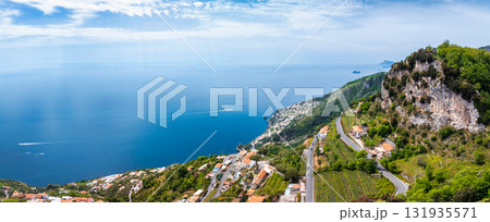 Aerial view of Amalfi, Italy, featuring cliffs, terraced vineyards, winding roads, white buildings, the Tyrrhenian Sea, small islands, and boats. 131935571