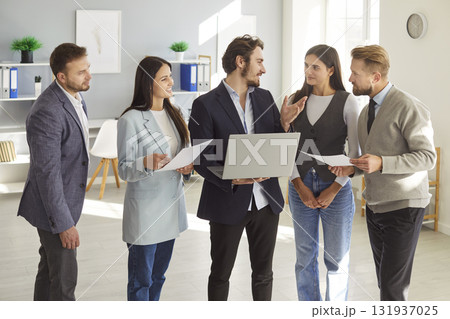 Group of company employees discussing work project on laptop standing in office during a meeting 131937025