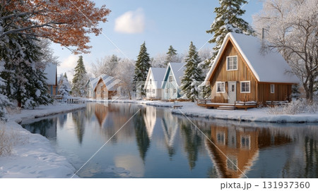 A serene winter village with snow covered cabins reflected in a calm frozen lake 131937360