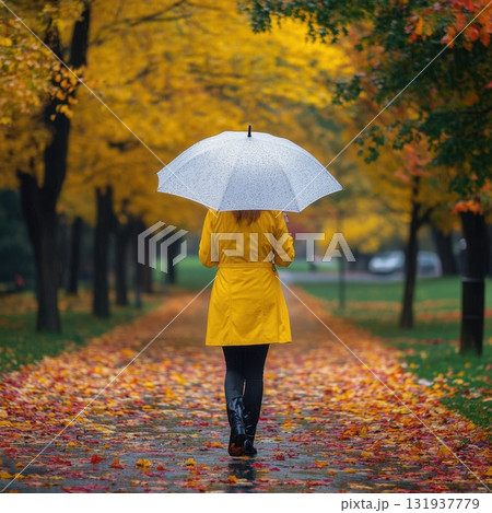 Bright yellow raincoat contrasts with autumn leaves on a rainy day in a city park 131937779
