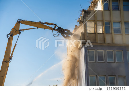 Powerful demolition of a concrete office building with a yellow high-reach excavator. Concept of transformation, destruction and construction renewal. Powerful demolition of a concrete office building with a yellow high-reach excavator. Concept of transformation, destruction and construction renewal. 131939351