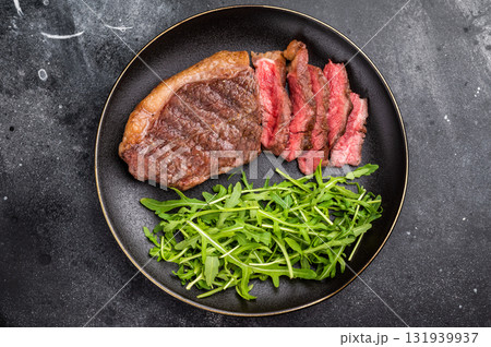 Appetizing grilled striploin steak with salad, inviting you to indulge in a mouthwatering culinary experience. black background. top view Appetizing grilled striploin steak with salad, inviting you to indulge in a mouthwatering culinary experience. black background. top view 131939937