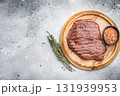Perfectly grilled top sirloin steak, seared to a juicy finish and garnished with fresh herbs for an irresistible flavor. grey background. top view 131939953