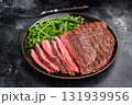 Juicy grilled top sirloin on a plate, accompanied by seasonal greens for a delicious meal. black background. top view 131939956
