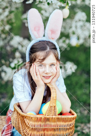 Easter egg hunt. Girl child Wearing Bunny Ears Running To Pick Up Egg In Garden. Easter tradition. Baby with basket full of colorful eggs. 131940725