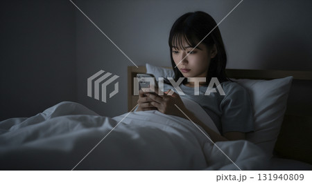 部屋着でベッドに寝転がりスマホを操作する女性 131940809