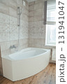 Corner acrylic bathtub with plastic front panel underneath in a bathroom with a window 131941047