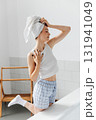 Cheerful attractive woman with a towel wrapped around her head posing in bathroom 131941049