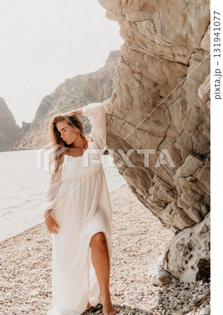 Woman White Dress Beach Rock - A woman wearing a white dress stands by a rocky cliff on a beach. 131941077